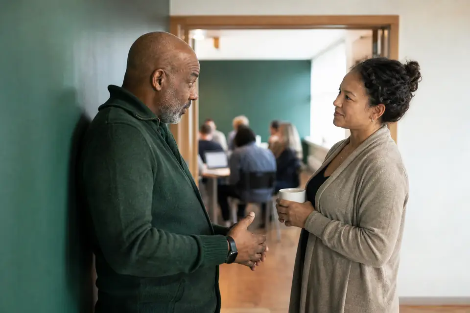Two nonprofit board members talking in a community center hallway outside a meeting.